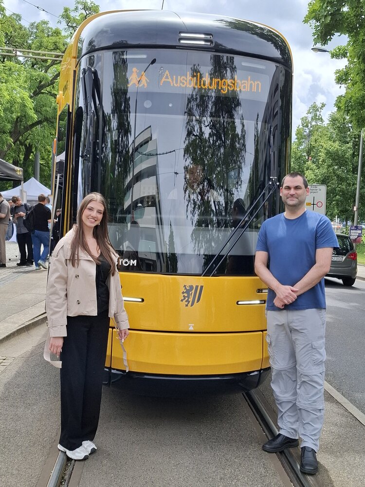 Eine Frau und ein Mann stehen vor einer Straßenbahn mit der Aufschrift "Ausbildungsbahn".