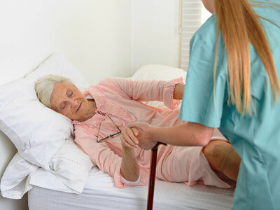 Auf dem Bild sieht man eine Person in türkiser Kleidung, die einer anderen Person auf einem Bett hilft und deren Fuß hält. Es veranschaulicht die Bedeutung von Fürsorge und Unterstützung im Gesundheitswesen.