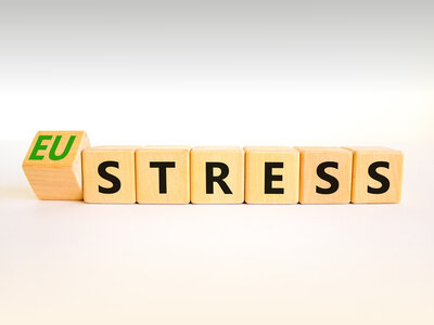 Holzblöcke mit Buchstaben, die das Wort 'EU STRESS' bilden. Der Block mit den Buchstaben 'EU' ist grün und steht leicht versetzt von den anderen Blöcken, die das Wort 'STRESS' in schwarzen Buchstaben zeigen. Die Blöcke sind auf einem hellen Hintergrund platziert.