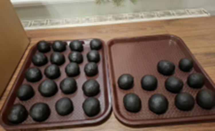 Zwei Tabletts auf einem Holztisch, darauf liegen in Reihen mehrere gleichmäßige schwarze Kugeln aus Räuchermasse zum Trocknen bereit.
