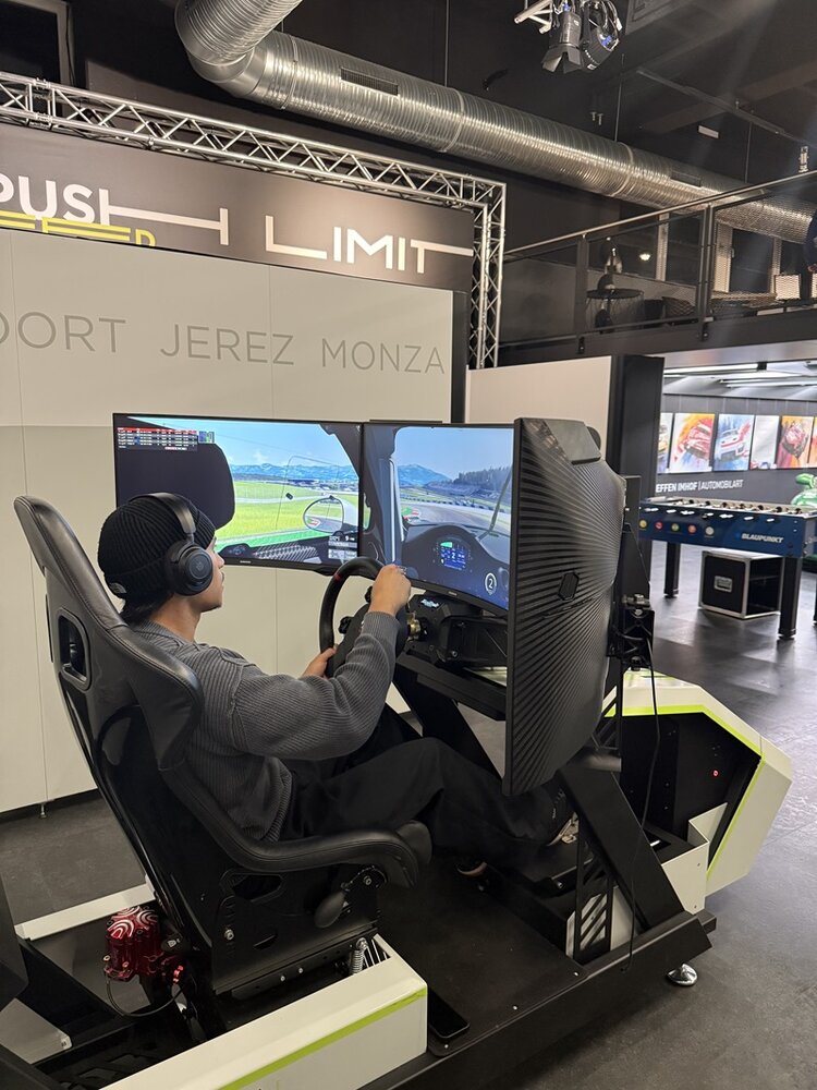Ein junger Mitarbeiter der ESO Education Group steuert während der Weihnachtsfeier einen High-End-Rennsimulator bei der ZEEEM eSports GmbH. Er sitzt in einem verstellbaren Racing-Seat mit Force-Feedback-Lenkrad und großen Curved-Screens. Im Hintergrund sind Industrie-Elemente, Beleuchtung und der Schriftzug „Push the Limit“ zu sehen, was die sportliche Atmosphäre unterstreicht.