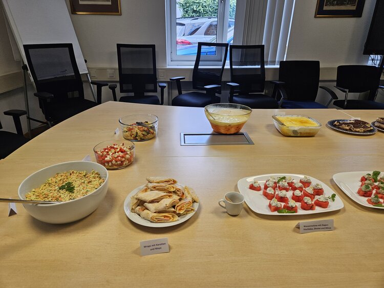 Auf einem Tisch sind verschiedene Speisen aufgestellt, wie kleine Schnittchen, Tomate-Mozzarella-Spieße und Schokokuchen.