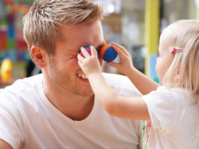 Ein Mädchen hält ihrem Kinderpfleger zwei bunte, kleine Bälle vor die Augen.