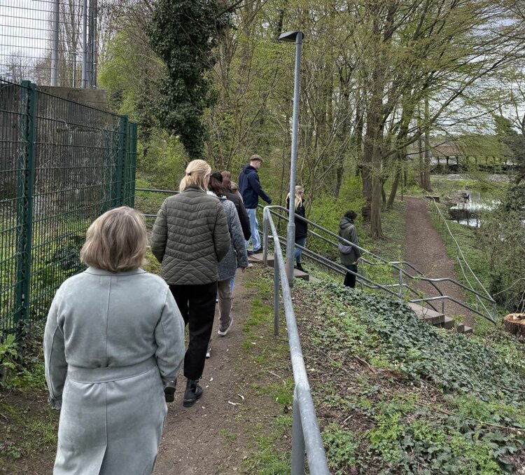 Achtsamtkeit im Fokus: ESO Education Group veranstaltet erneut erfolgreichen Gesundheitstag in Stockstadt Eine Gruppe von Menschen geht einen Weg entlang, der von einem Zaun und Bäumen gesäumt ist. Der Weg führt zu einer Treppe, die zu einem tiefer gelegenen Bereich hinaufführt.
