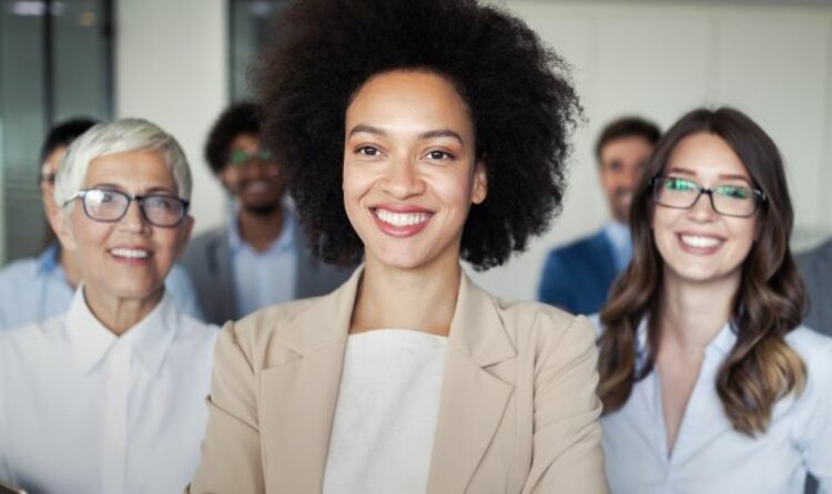 Eine diverse Gruppe von lächelnder Geschäftsleute, in der eine Frau im Vordergrund steht. 
