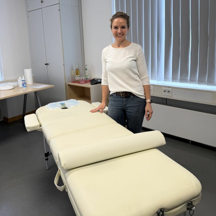Achtsamtkeit im Fokus: ESO Education Group veranstaltet erneut erfolgreichen Gesundheitstag in Stockstadt Eine Person steht lächelnd in einem Raum mit einer Massageliege. Im Hintergrund sind ein Tisch mit Utensilien und ein Fenster mit geschlossenen Vorhängen zu sehen.