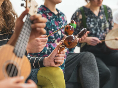 Das Bild zeigt eine Gruppe von Menschen, die verschiedene Musikinstrumente wie Ukulele, Perkussion, Maracas, Rahmentrommel, spielen. Alle Personen der Musikgruppe tragen lässige Kleidung und scheinen sich in einer entspannten Umgebung in einer Freizeitaktivität zu befinden.