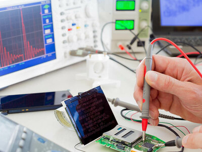 Eine Person verwendet ein Multimeter, um Komponenten auf einer elektronischen Leiterplatte zu testen oder zu messen. Die Umgebung umfasst verschiedene elektronische Geräte wie ein Oszilloskop mit sichtbaren Wellenformen, ein Netzgerät mit digitalen Anzeigen und weitere typische Werkzeuge eines Elektroniklabors.