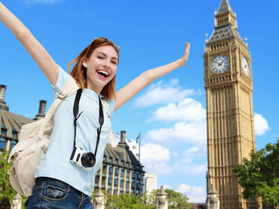 Eine Person steht mit erhobenen Armen vor dem Big Ben in London. Sie trägt ein hellblaues Hemd, Jeans, einen weißen Rucksack und eine Kamera um den Hals. Der Himmel ist blau mit einigen Wolken.