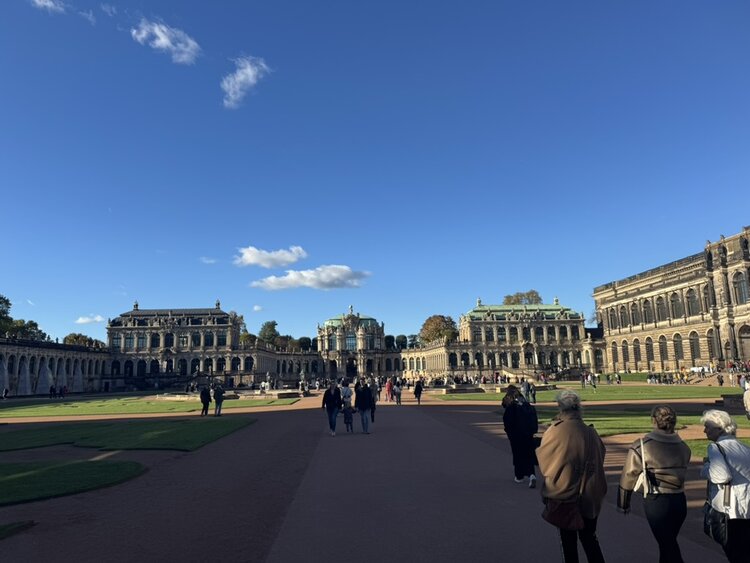 Ein Wiedersehen in Dresden – 9. ESO-Seniorentreffen mit Wein, Geschichte und guter Laune Großer, sonniger Platz mit historischem Barockbau - dem Dresdner Zwinger. Symmetrische Gebäude mit Arkadengängen, Säulen und grünem Kuppeldach. Menschen spazieren auf Wegen und Rasenflächen bei klarem blauen Himmel.