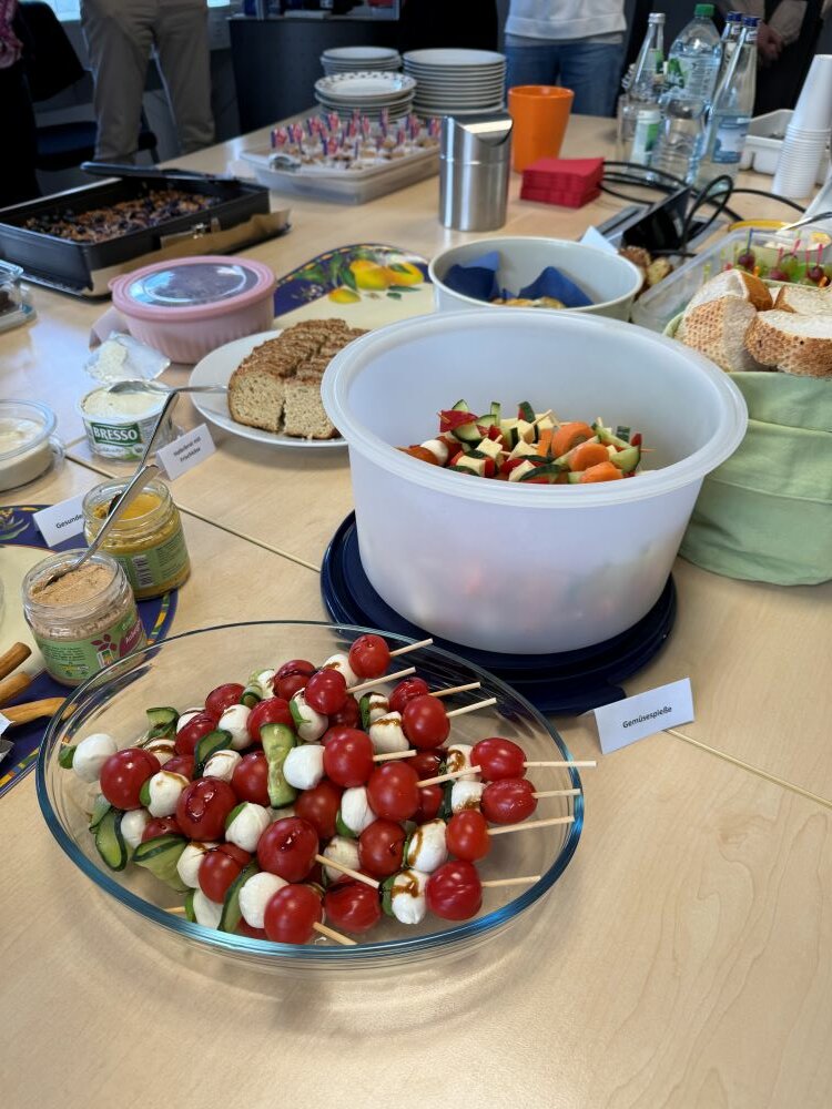 Achtsamtkeit im Fokus: ESO Education Group veranstaltet erneut erfolgreichen Gesundheitstag in Stockstadt Ein Tisch mit verschiedenen Snacks, darunter ein Teller mit Gemüsesticks und Dip, sowie ein Glas mit Caprese-Spießen aus Tomaten, Mozzarella und Basilikum.