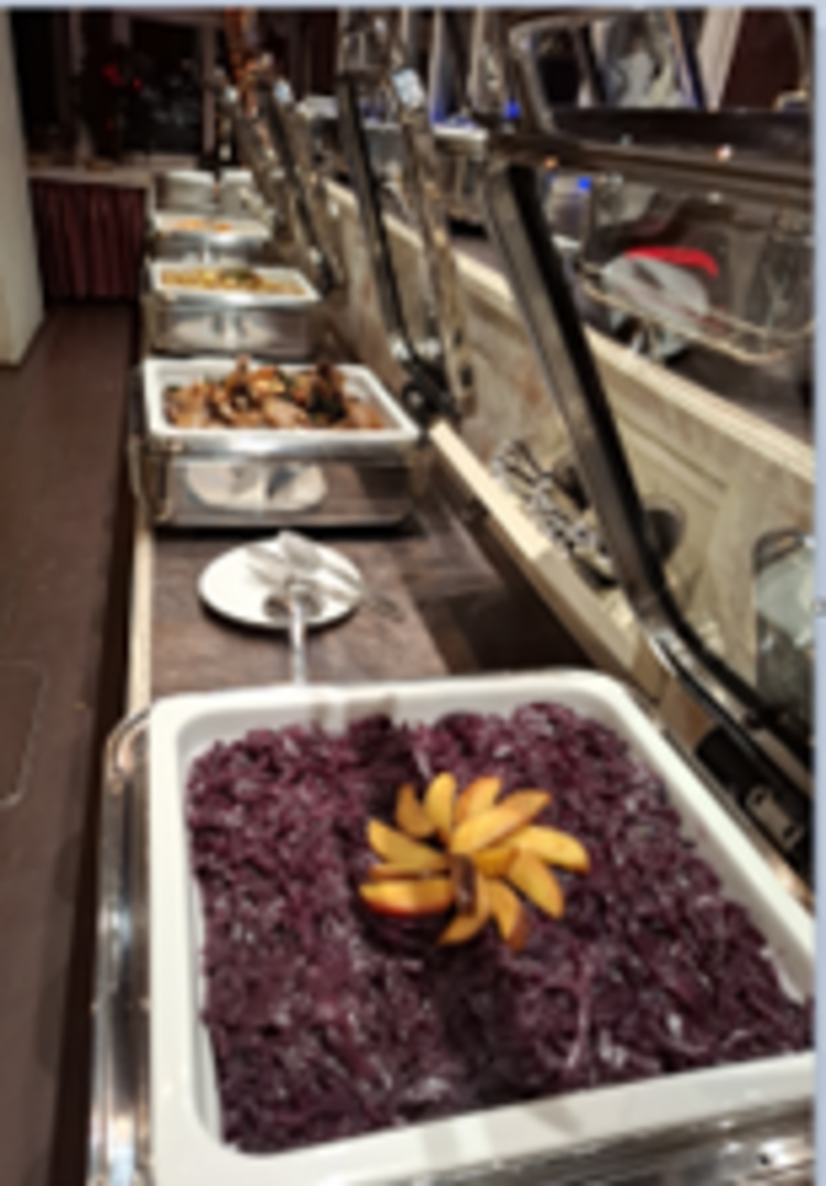 Buffettheke mit mehreren Edelstahlschalen, vorne Rotkohl mit dekorativ aufgefächerten Apfelscheiben, dahinter weitere warme Speisen.
