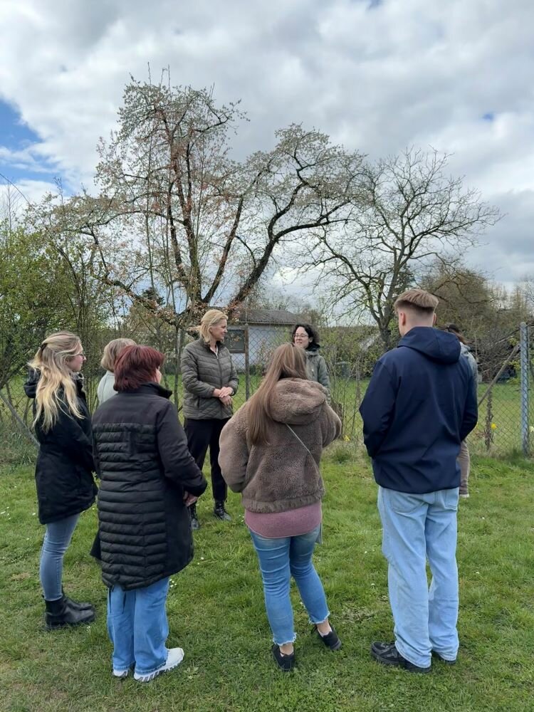 Achtsamtkeit im Fokus: ESO Education Group veranstaltet erneut erfolgreichen Gesundheitstag in Stockstadt Eine Gruppe von Menschen steht im Freien auf einer Wiese und hört aufmerksam einer Person zu, die zu ihnen spricht. Im Hintergrund sind Bäume und ein Zaun zu sehen.