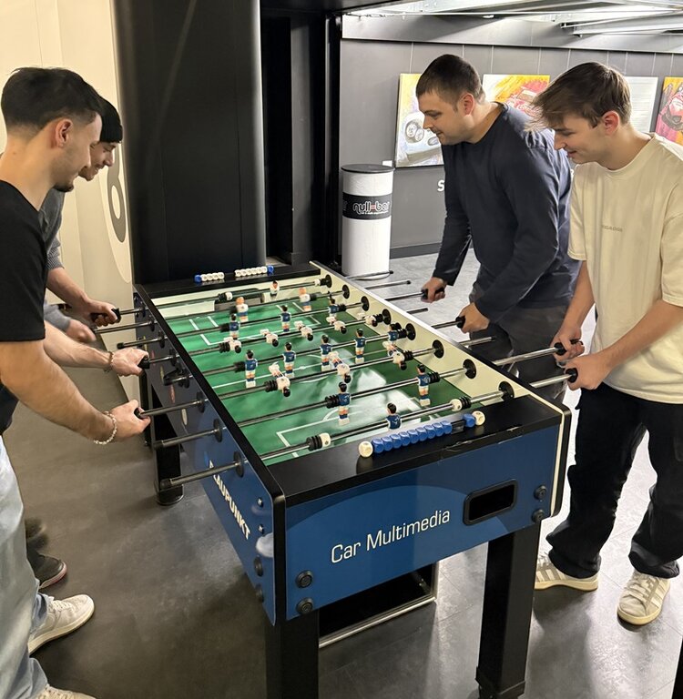 Vier Mitarbeitende der ESO Education Group spielen bei der Weihnachtsfeier 2025 gemeinsam Tischkicker bei der ZEEEM eSports GmbH. Sie stehen konzentriert an einem blau-schwarzen Kickertisch mit der Aufschrift „Car Multimedia“. Die Szene vermittelt Teamgeist, Spaß und lockere, soziale Interaktion in moderner Eventlocation.