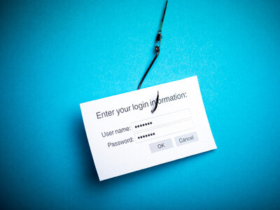 Ein weißes Blatt Papier mit einem Login-Formular ist an einem Angelhaken befestigt. Das Formular enthält Felder für Benutzername und Passwort sowie die Schaltflächen 'OK' und 'Abbrechen'. Der Hintergrund ist blau.