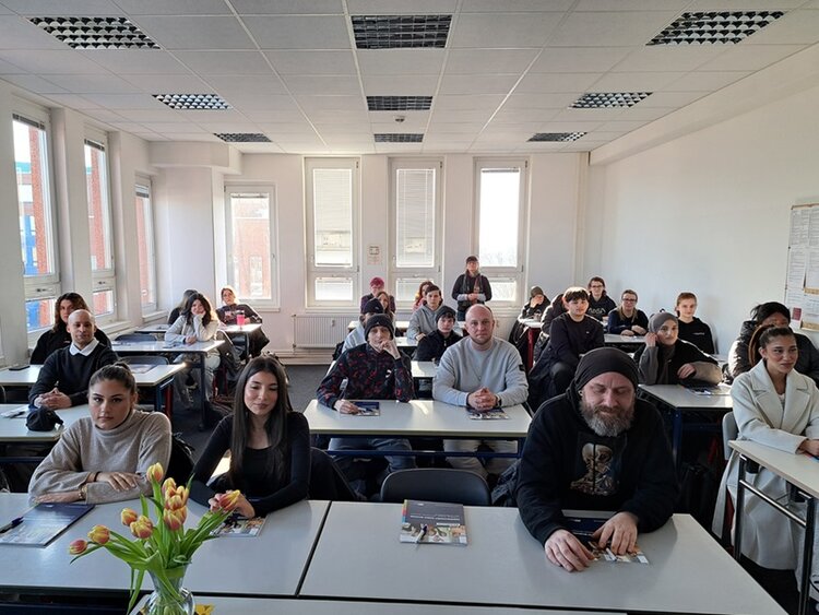 Die neuen Auszubildenden zu Sozialassistentinnen und Sozialassistenten sitzen im Klassenraum an Tischen und posieren für ein Gruppenfoto.