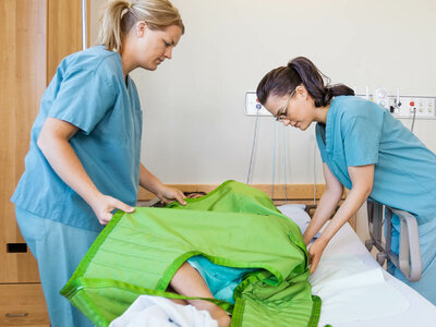 Zwei Pflegerinnen wenden einen Patienten in einem Krankenbett.