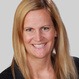 Die Funktionsbereichsleitung Human Resources, Eva Krug, mit blonden langen Haaren lächelt auf diesem Portrait vor grauem Hintergrund freundlich in die Kamera.
