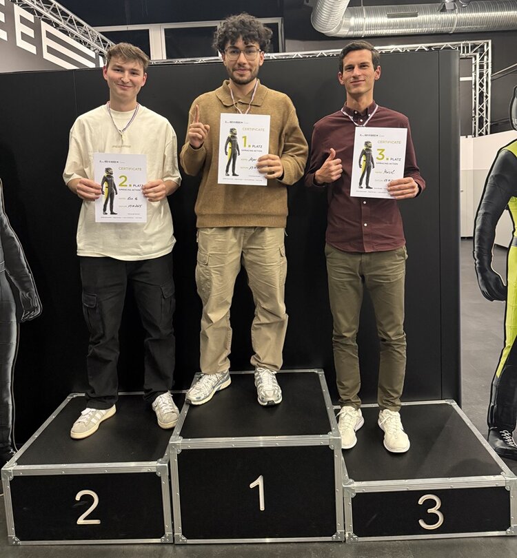 Drei junge Mitarbeitende der ESO Education Group stehen bei der Weihnachtsfeier auf einem Siegerpodest der ZEEEM eSports GmbH. Sie halten Urkunden in den Händen und tragen Medaillen, die ihre Platzierungen 1, 2 und 3 im Rennsimulator-Wettbewerb auszeichnen. Alle drei lächeln und zeigen stolz ihre Urkunde in die Kamera, während schwarze Wände und metallische Eventtechnik den Hintergrund bilden.