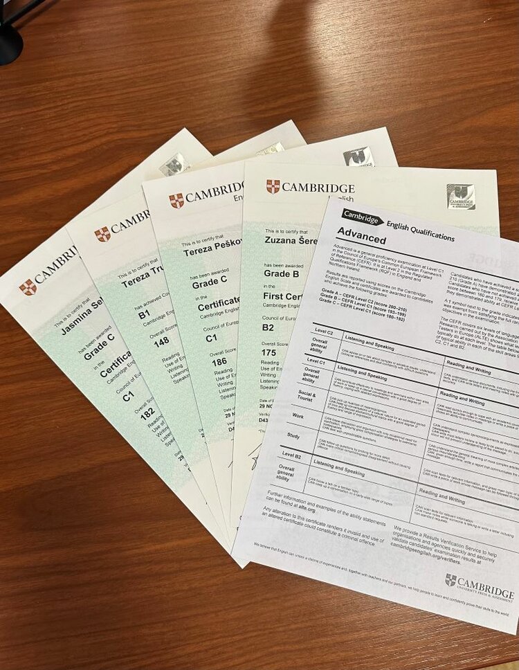 Mehrere Cambridge Englisch-Zertifikate liegen auf einem Tisch. Die Zertifikate sind grün-weiß und zeigen das Logo der Universität Cambridge. Auf den Zertifikaten sind Namen und erreichte Noten (z. B. Grade C, B1, B2) zu erkennen.
