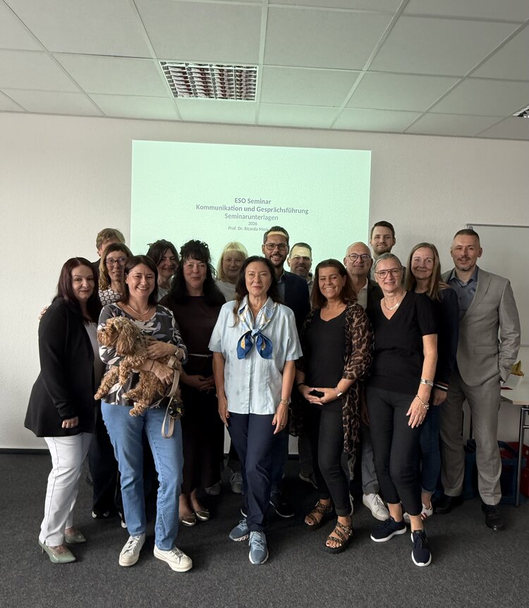 Kommunikation als Schlüssel nachhaltiger Führung Teilnehmende des Kommunikationstrainings der ESO Education Group stehen für ein Gruppenfoto in den Räumlichkeiten der Euro Akademie Aschaffenburg vor einer Präsentationsfolie zusammen.