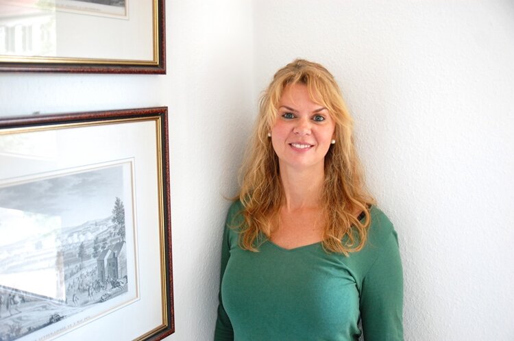 ESO Education Group Mitarbeiterin Monique Glaser trägt ein grünes Langarmoberteil mit Rundhalsausschnitt und posiert lächelnd, mit halb offenen blonden, langen und gewellten Haaren, für ein Bild im hellen Treppenhaus.