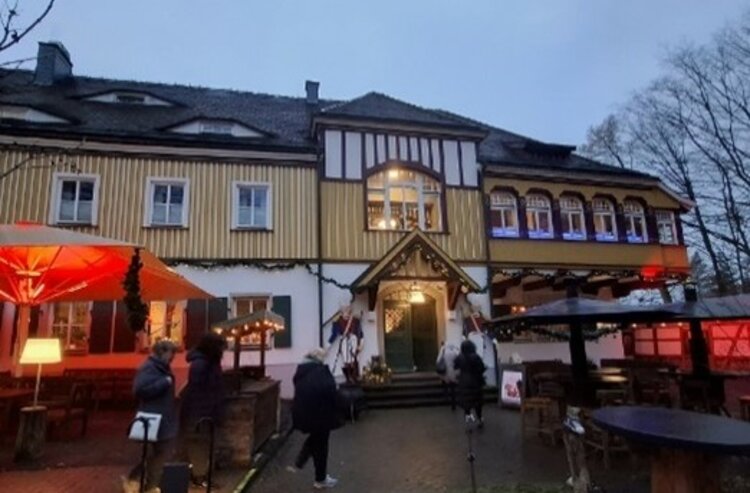 Abendliche Außenansicht des „Historischen Fischhauses“ mit beleuchtetem Eingang, Fachwerkfassade und Gästen, die über den Hof mit roten Schirmen zum Gebäude gehen.