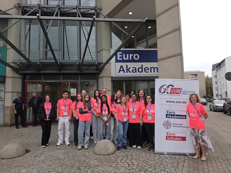 Gemeinsam im Einsatz für die PingPongParkinson-WM 2026 Gruppe von Teilnehmenden in pinken T-Shirts vor dem Gebäude der Euro Akademie neben einem Banner der ESO Education Group.