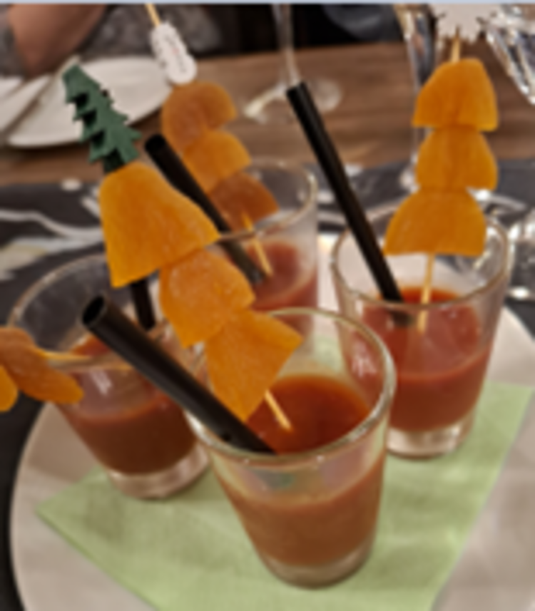 Kleine Gläser mit roter Suppe oder Drink, in denen schwarze Trinkhalme und Holzspieße mit in Stücke geschnittenen getrockneten Aprikosen stecken, auf einer grünen Serviette angerichtet.