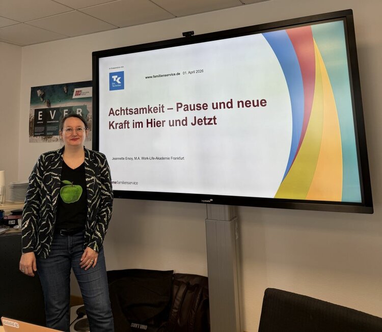 Achtsamtkeit im Fokus: ESO Education Group veranstaltet erneut erfolgreichen Gesundheitstag in Stockstadt Eine Person steht lächelnd vor einem Bildschirm, auf dem eine Präsentation mit dem Titel „Achtsamkeit – Pause und neue Kraft im Hier und Jetzt“ zu sehen ist. Der Bildschirm zeigt auch das Datum 01. April 2026 und den Namen Jeannette Ersoy, M.A., Work-Life-Akademie Frankfurt.
