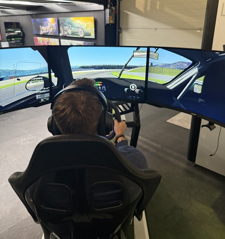 Teilnehmender der ESO Education Group sitzt bei der Weihnachtsfeier 2025 in einem professionellen Rennsimulator der ZEEEM eSports GmbH. Er trägt Kopfhörer und steuert auf drei großen, gebogenen Monitoren ein realistisches Autorennen mit Blick auf eine sonnige Rennstrecke. Die Szene zeigt ein immersives Gaming-Erlebnis in moderner eSports-Umgebung.