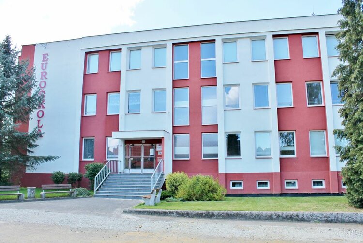Ein mehrstöckiges Schulgebäude mit der Aufschrift „EUROŠKOLA“ an der Fassade. Das Gebäude hat weiße und rote Farbakzente sowie mehrere Fenster. Vor dem Gebäude sind Bäume und ein gepflegter Rasen zu sehen.