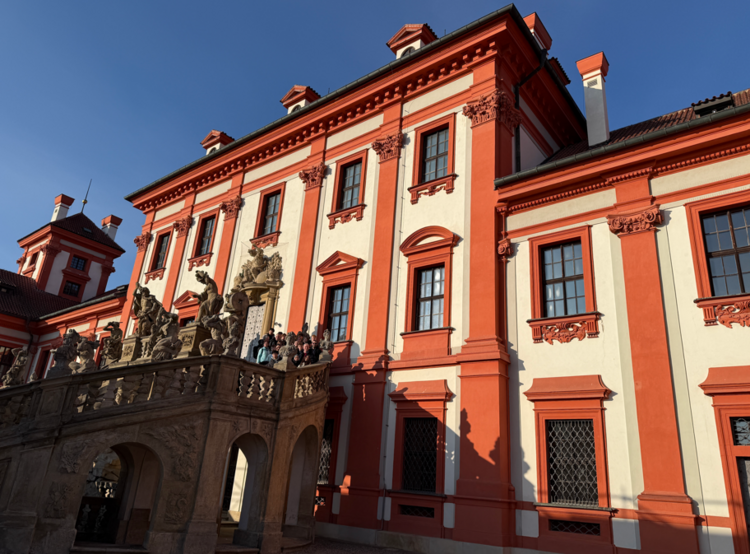 Ein Schloss steht im Halbschatten. Die Fassade ist mit rostbrauner Farbe und heller Farbe bemalt.