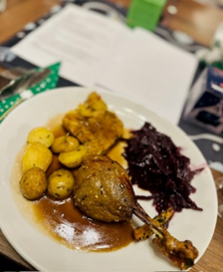 Hauptgericht auf einem weißen Teller mit knuspriger Gänsekeule, Bratkartoffeln, Rotkohl und brauner Soße, auf einem festlich gedeckten Tisch.