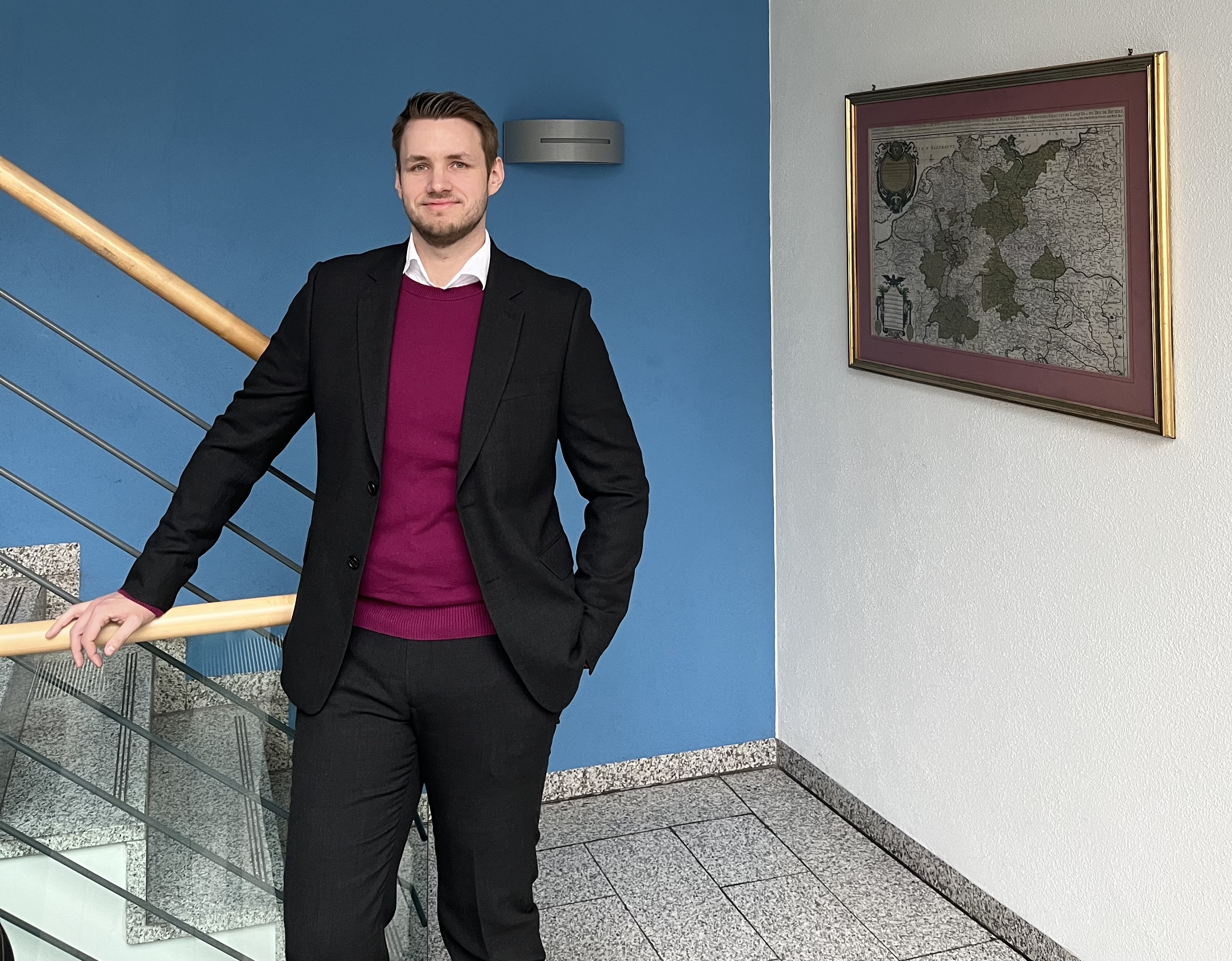 Jan Herfs der ESO Education Group steht mit einer schwarzen Hose, einem weinrotem Shirt und einer schwarzen Jacke in einem Treppenhaus.